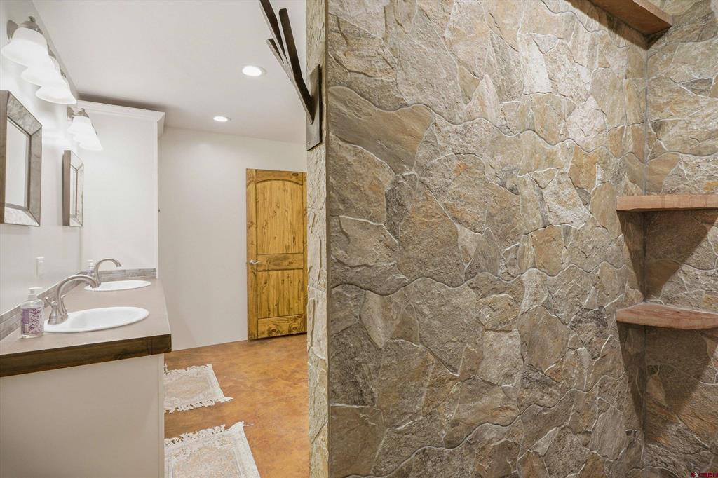 Bathroom with a double-sink vanity beside a stone-tiled wall with built-in shelves.