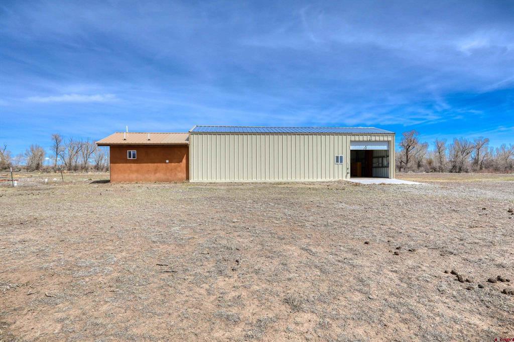 Reddish-brown stucco home attached to a long metal-sided building with an open bay on a wide, bare lot.