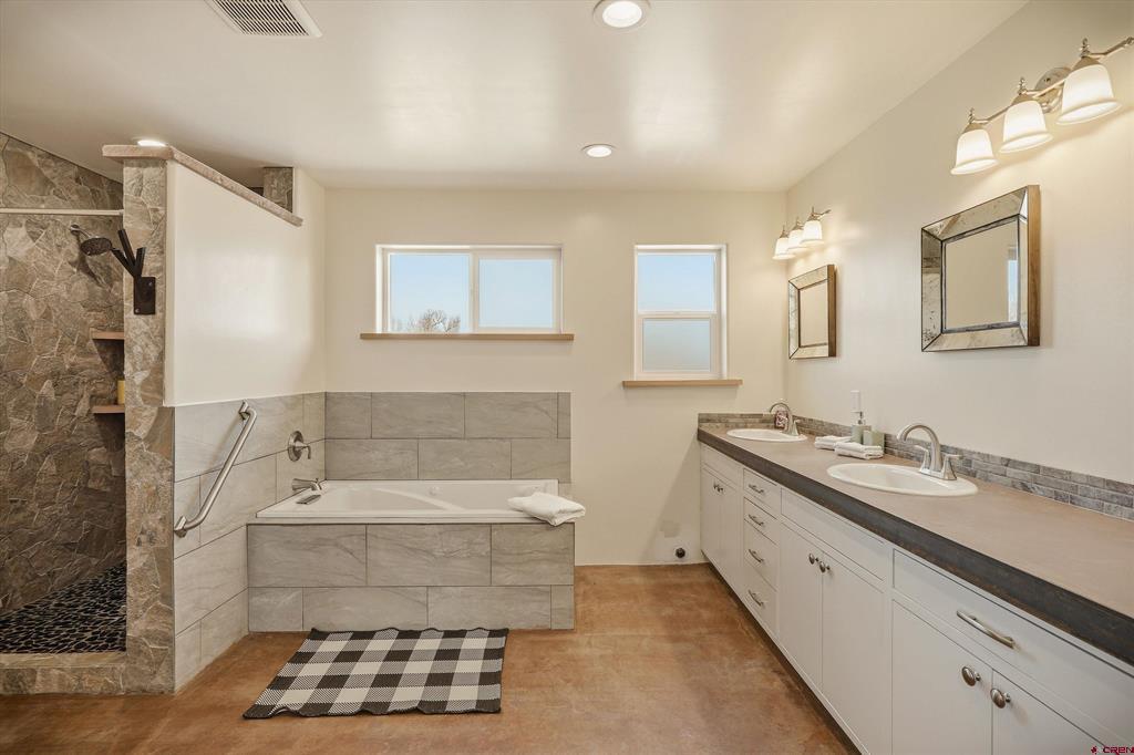 Spacious bathroom with a double vanity, tiled bathtub, and stone walk-in shower.