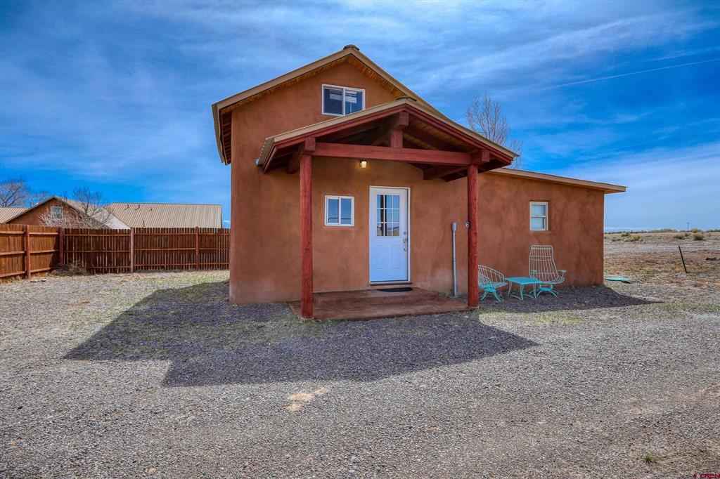 Brown stucco home with a covered red-wood porch, white entry door, and gravel yard.