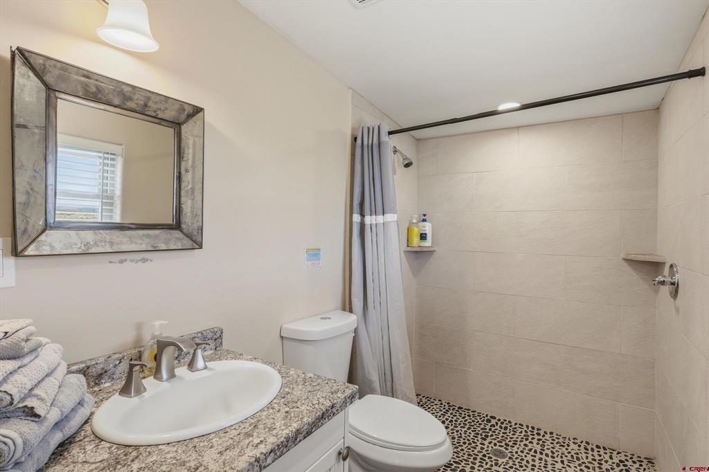 Bathroom with a granite vanity and a tiled walk-in shower with pebble-stone flooring.