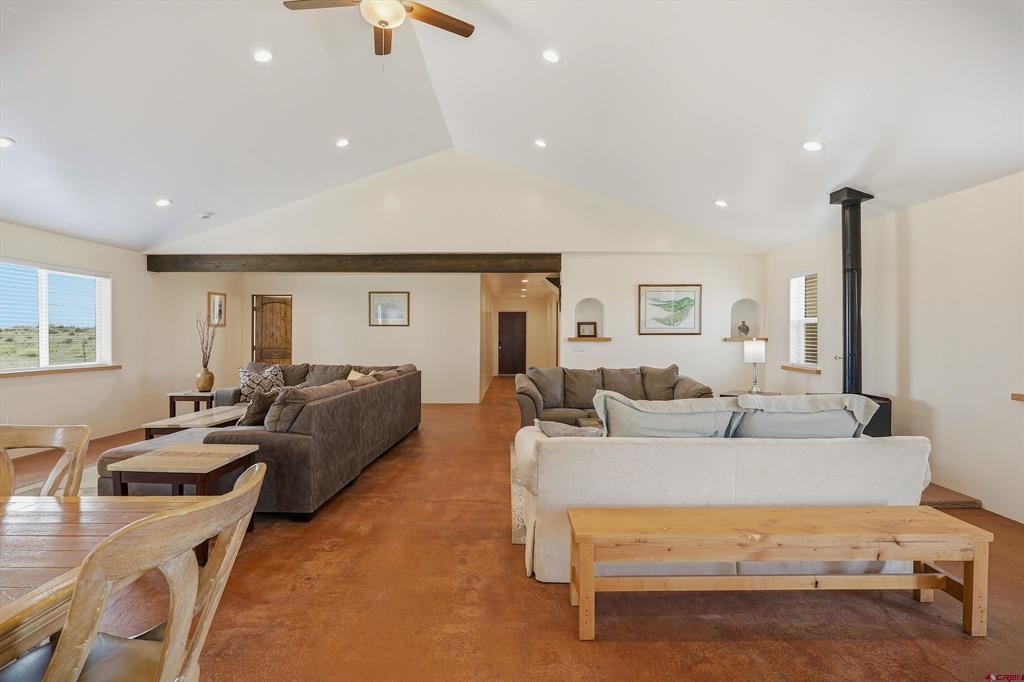 Furnished living room with a vaulted ceiling, exposed beam, and black wood-burning stove.