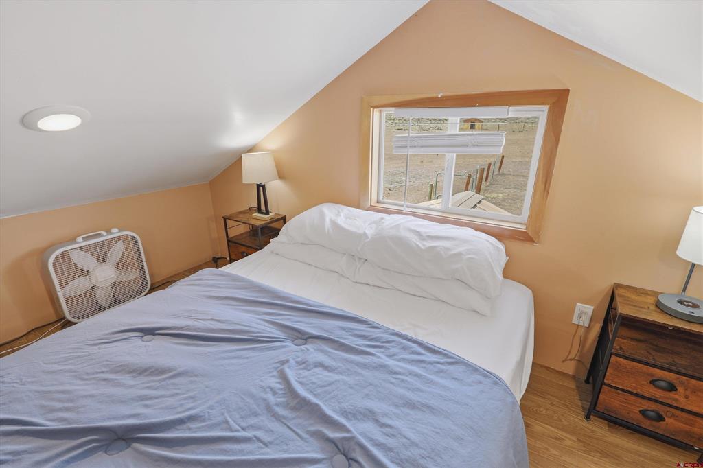 Bedroom with a bed beneath a sloped ceiling and a window overlooking a fenced yard.