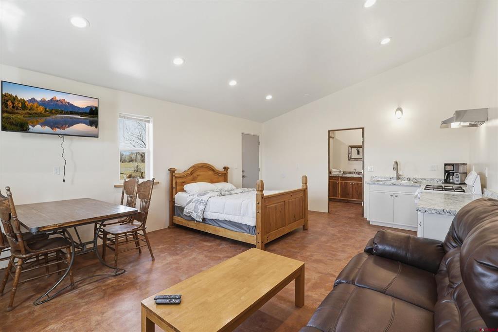 Furnished studio bedroom with a wooden bed, dining table, kitchenette, and leather sofa.