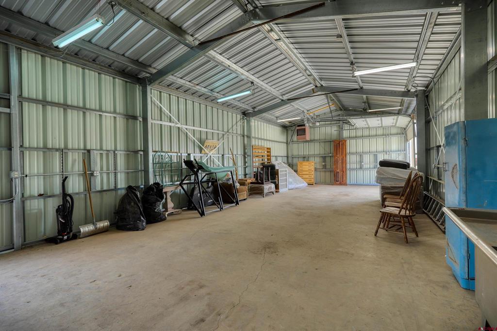 Large metal workshop with an open concrete floor and stored furniture and equipment along the walls.