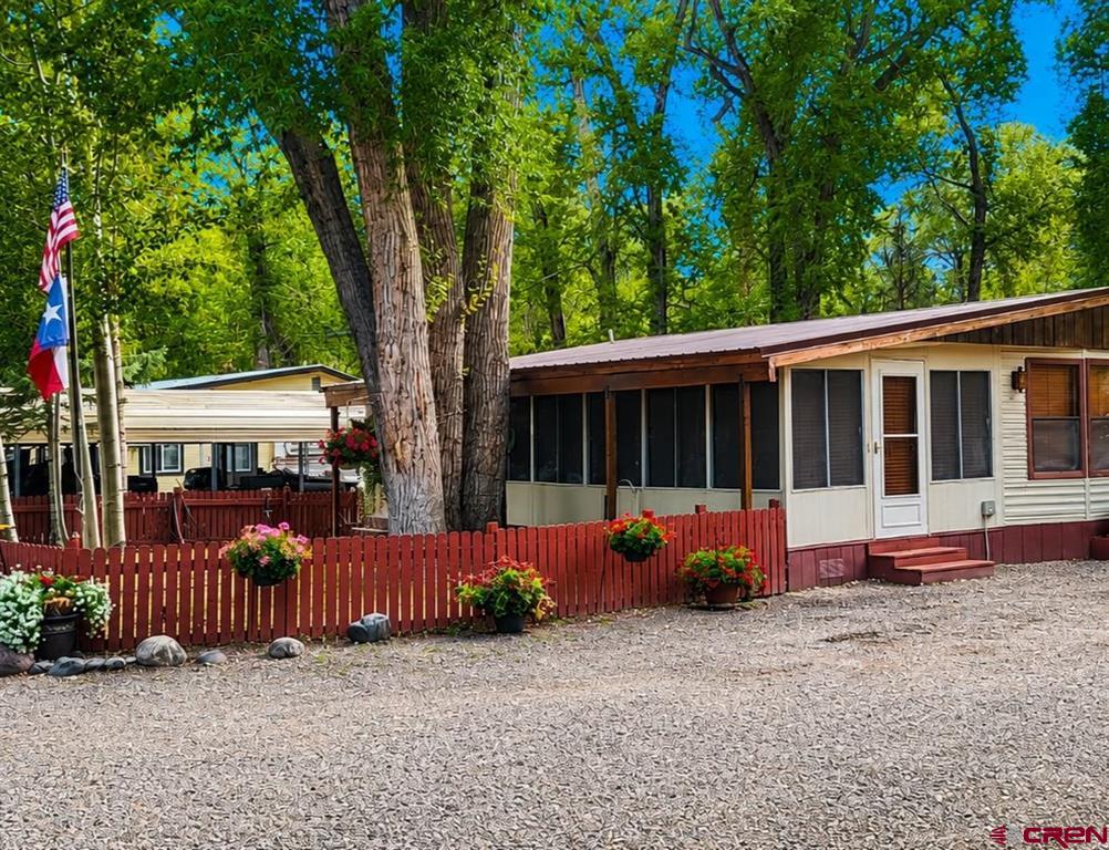Manufactured home with a screened porch behind a red picket fence and gravel yard.