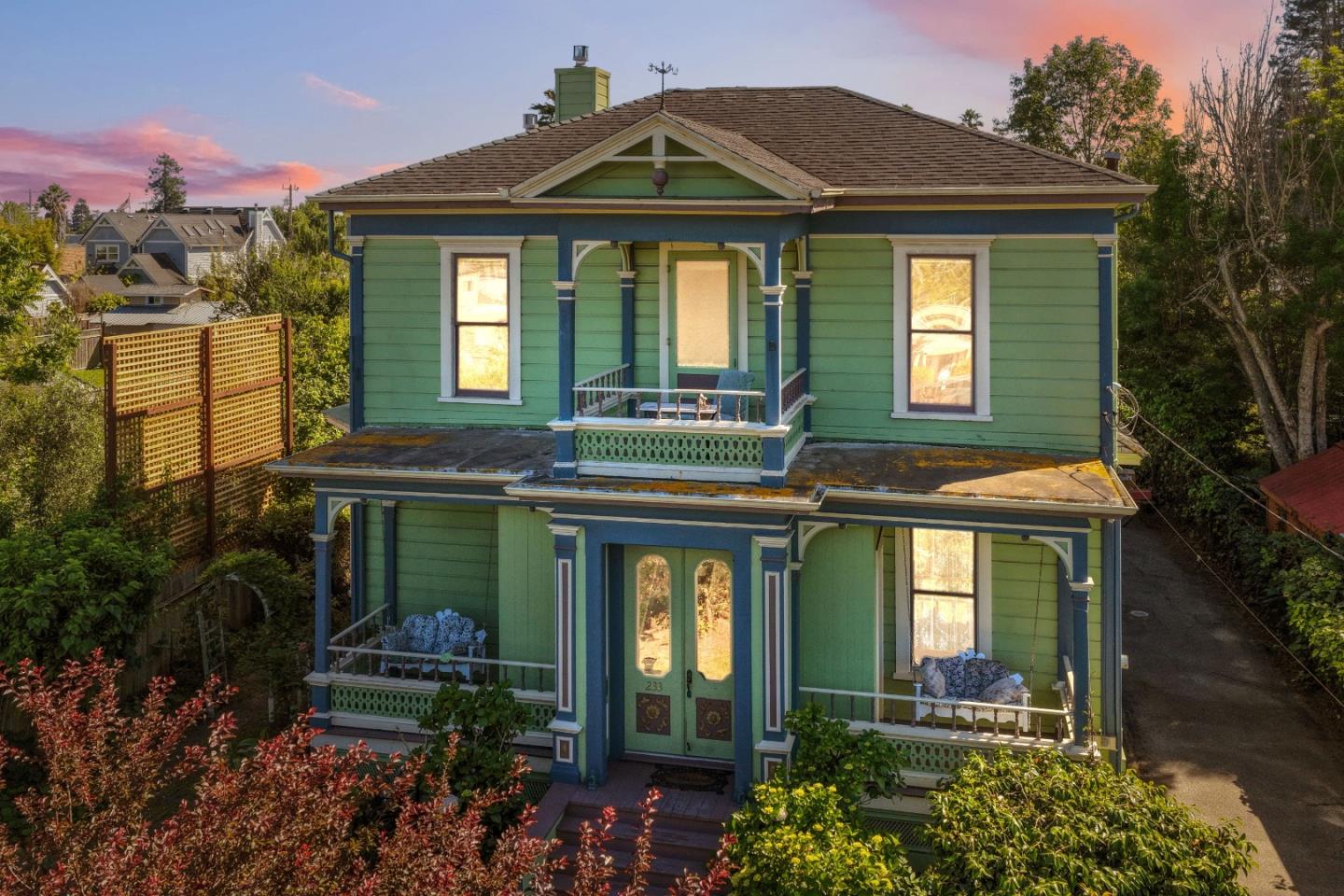 Green two-story house with blue trim and covered porches, photographed at sunset.