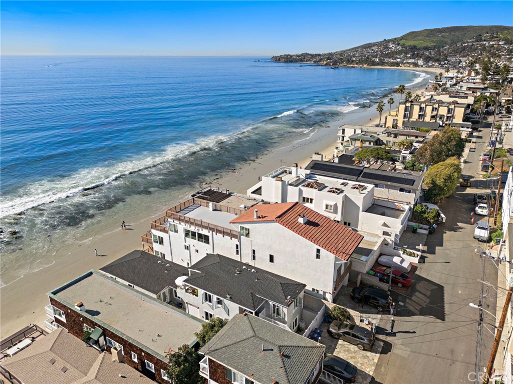 Beachfront homes along a curved Laguna Beach shoreline, with ocean waves and coastal hills.