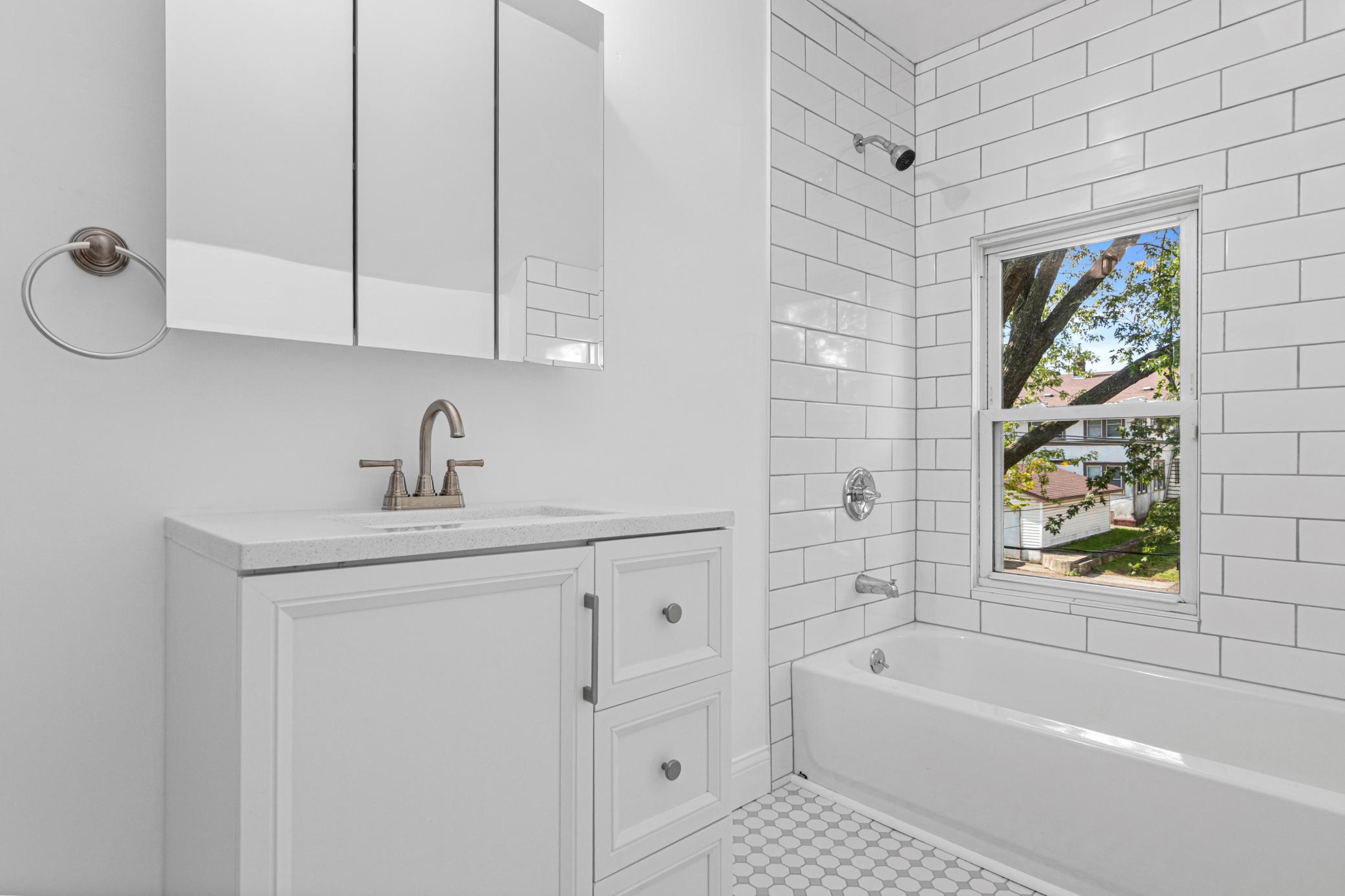 Bathroom with white subway tile, a bathtub beside a window, and a white vanity with mirrored cabinets.