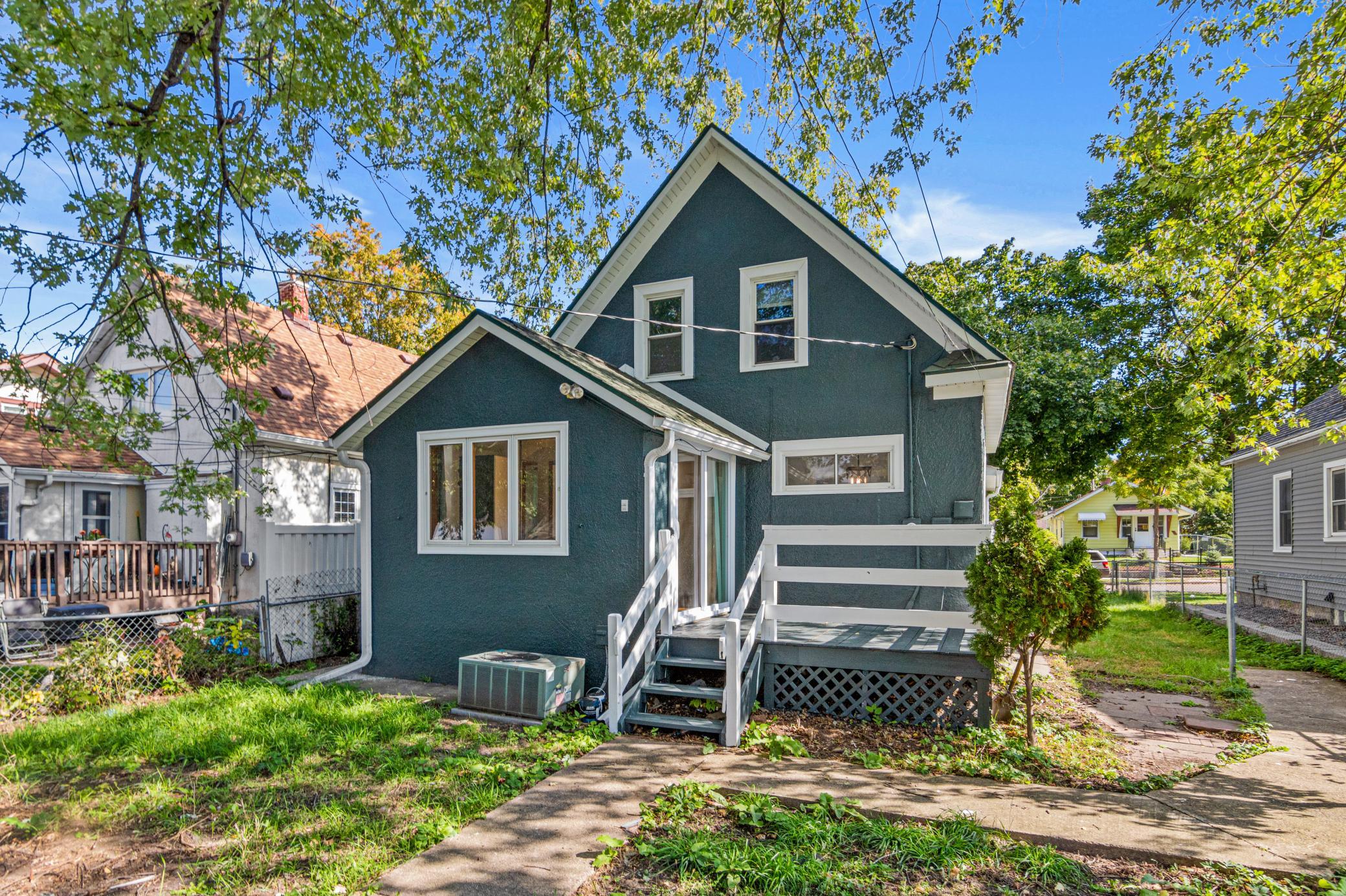 Rear of a dark teal two-story house with white-trimmed windows, raised deck, and leafy yard.