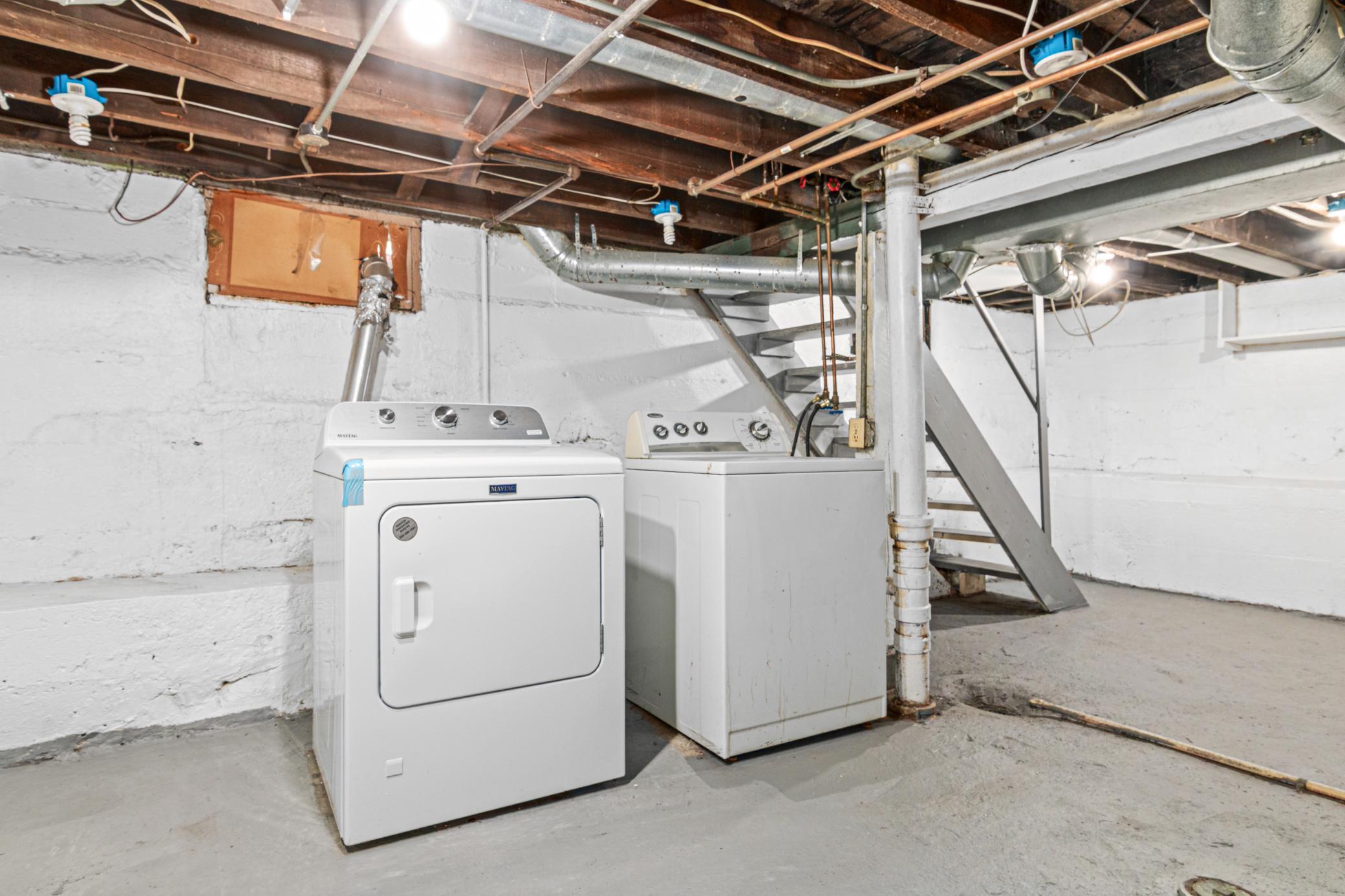 Basement laundry area with a Maytag washer and dryer beneath exposed joists and ductwork.