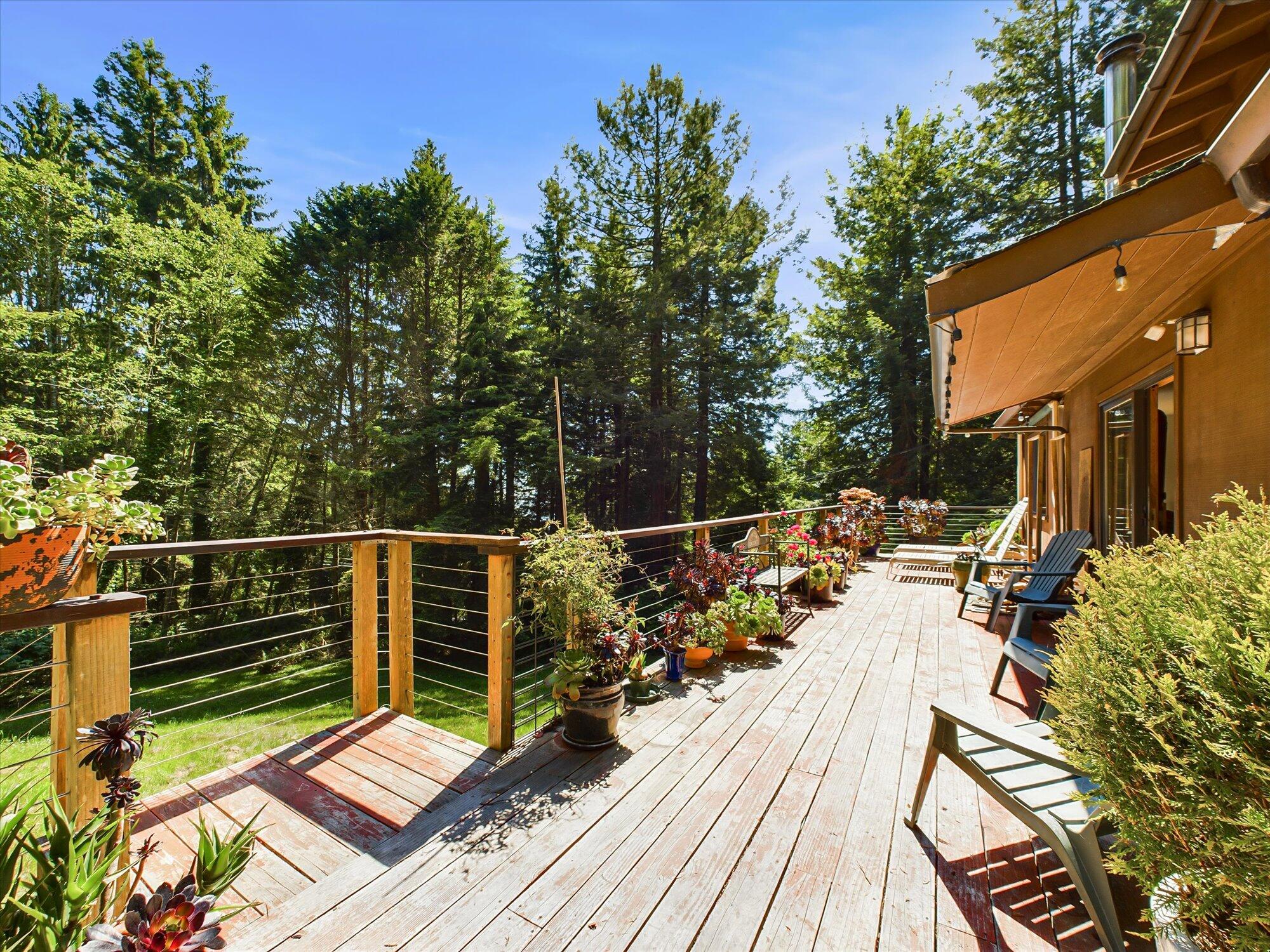Wooden home deck with cable railing, lounge chairs, and potted plants overlooking a forest.