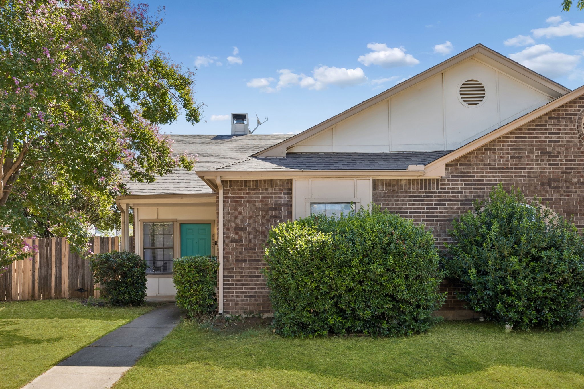 Brick house with a teal front door, white gable, and flowering tree beside the entrance.