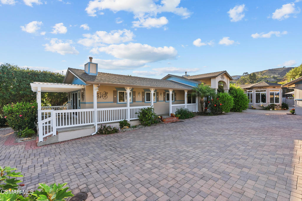 Single-story home with a long covered porch and broad paved courtyard.