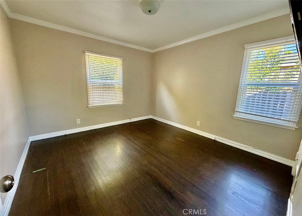 Empty room with dark hardwood floors, beige walls, and two windows with blinds.