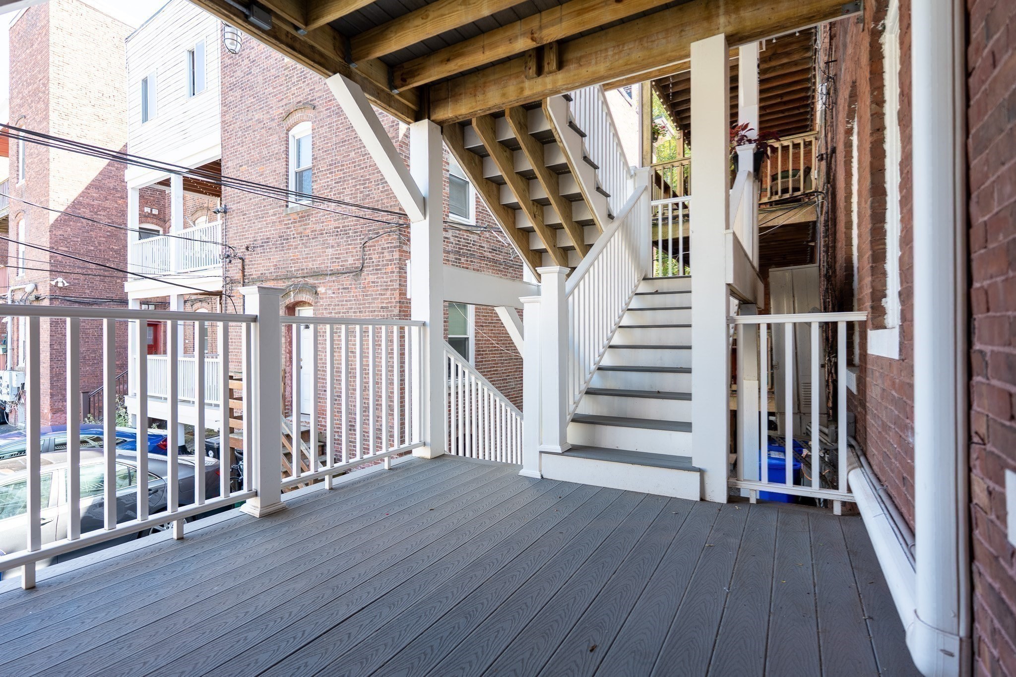 Covered porch with gray decking, white railings, and stairs beneath exposed timber beams.