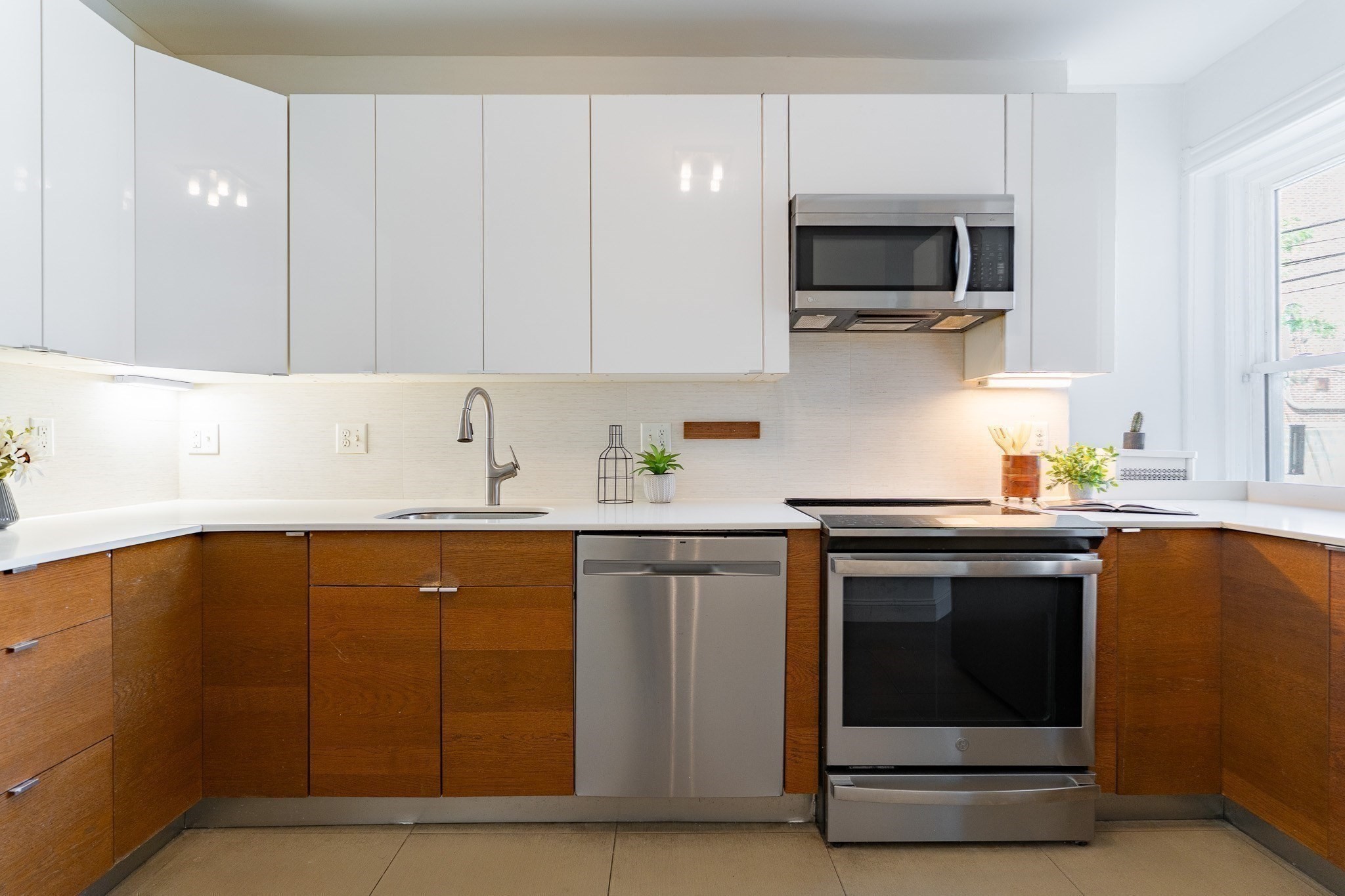 Modern kitchen with warm wood cabinets, stainless steel appliances, and a large window.