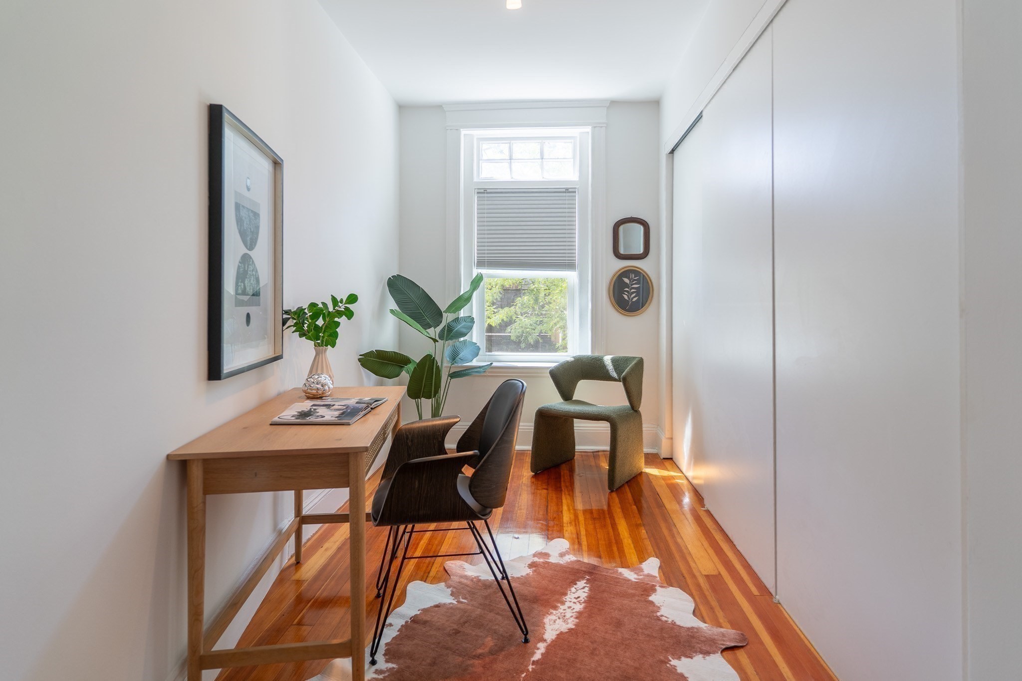 Home office with a wood desk, two chairs, leafy plants, and polished hardwood floors.