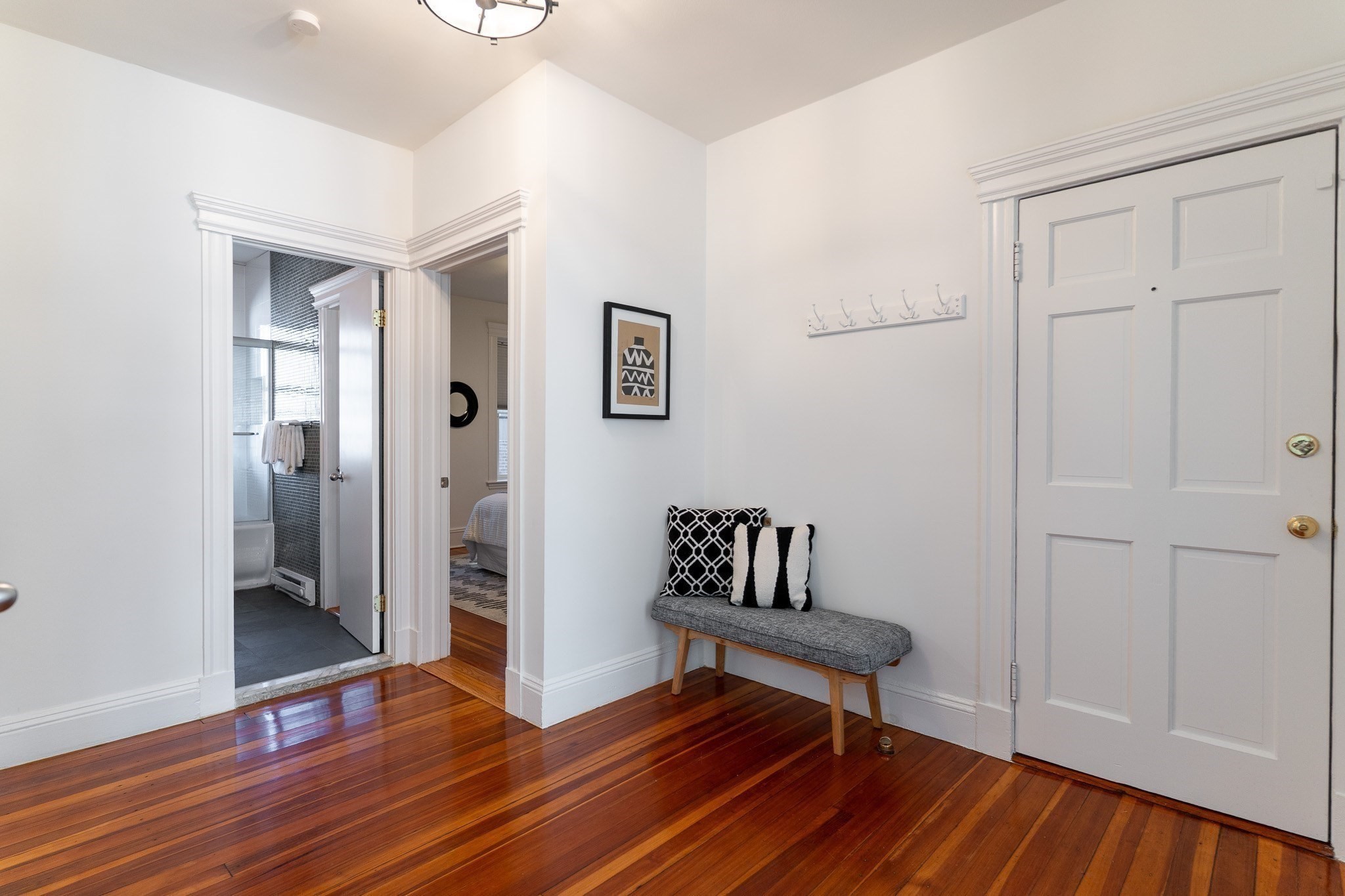 Apartment entryway with a white paneled door, hardwood floors, and a cushioned bench.
