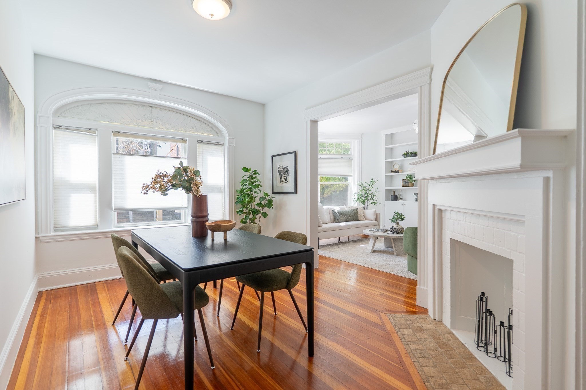 Dining room with a black table, arched bay window, and white brick fireplace beside an adjoining sitting room.