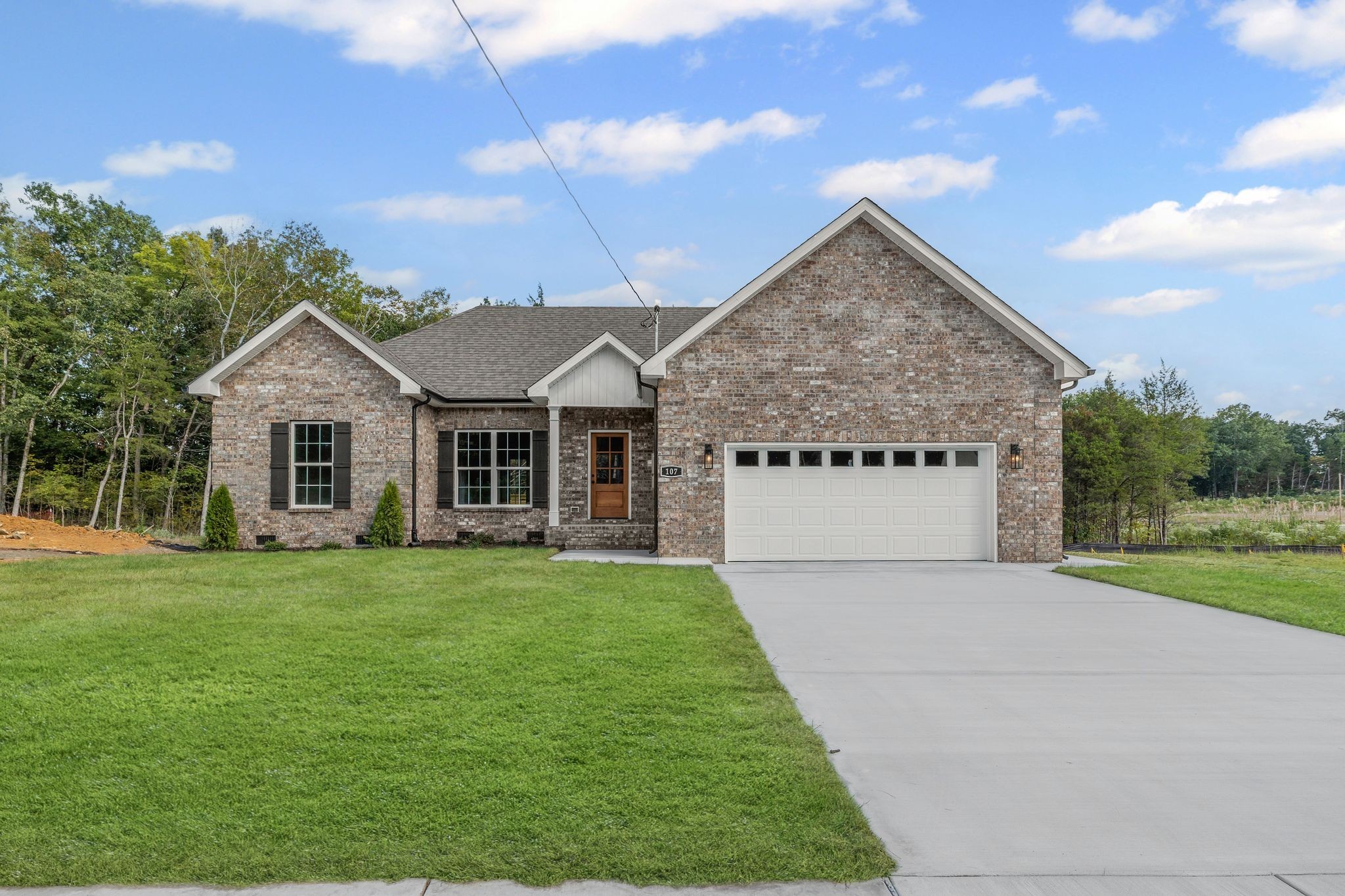 Brick house with gabled roof, white double garage door, and broad driveway bordered by a green lawn.