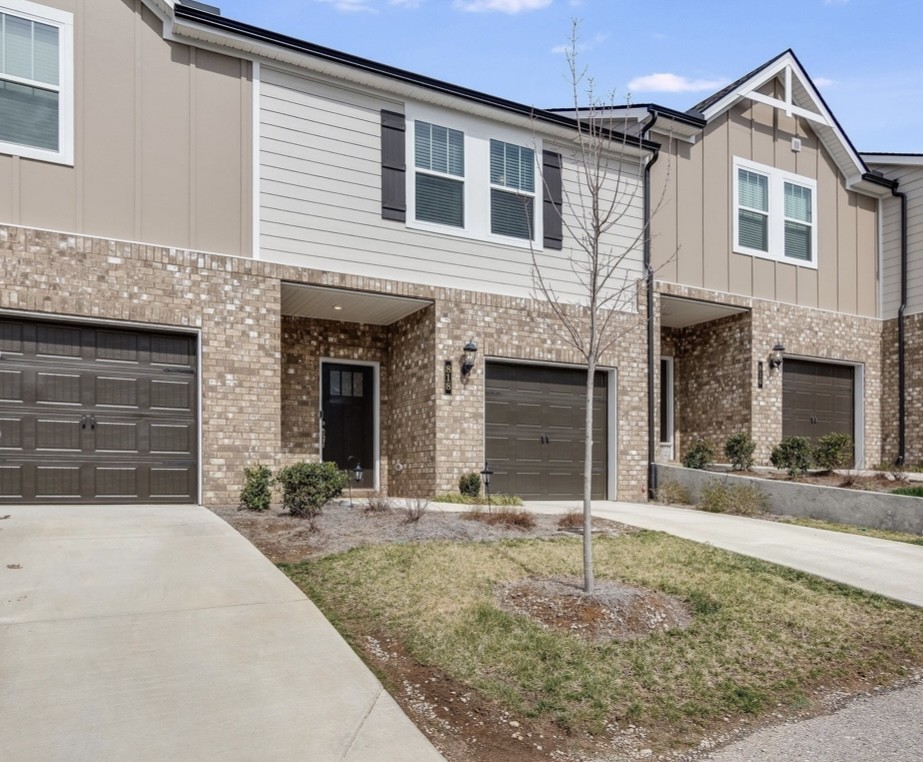 Attached two-story townhomes with brick façades, dark garage doors, and a leafless tree in front.