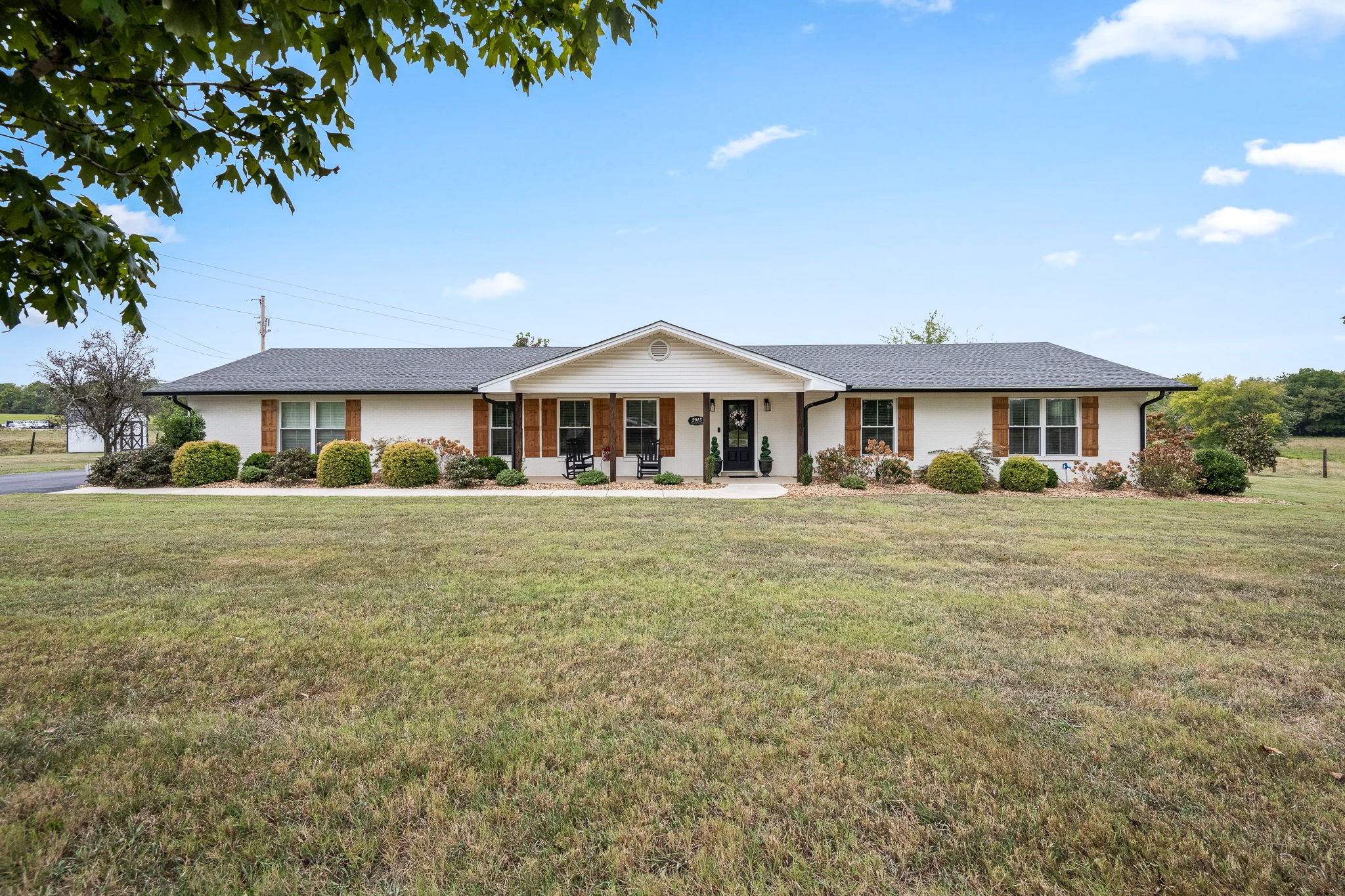 White ranch-style home with a covered porch, wooden shutters, and a broad front lawn.