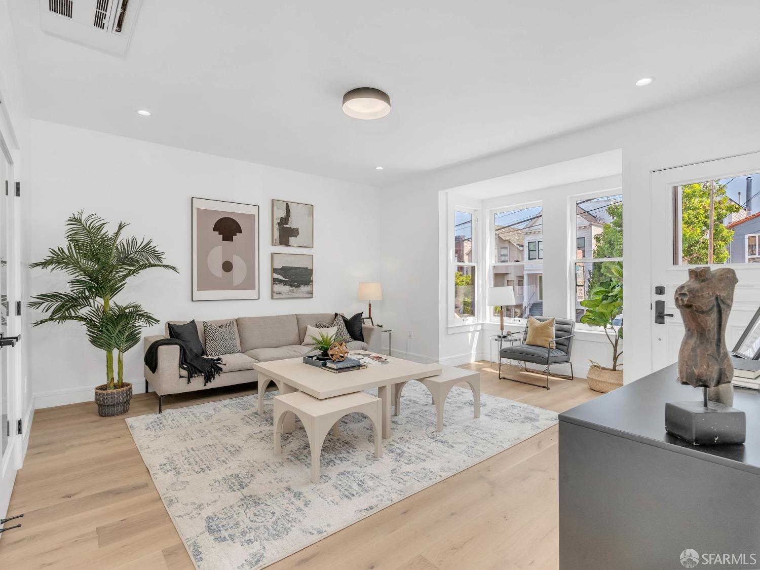 Bright staged living room with a beige sofa, pale wood floors, and large windows.