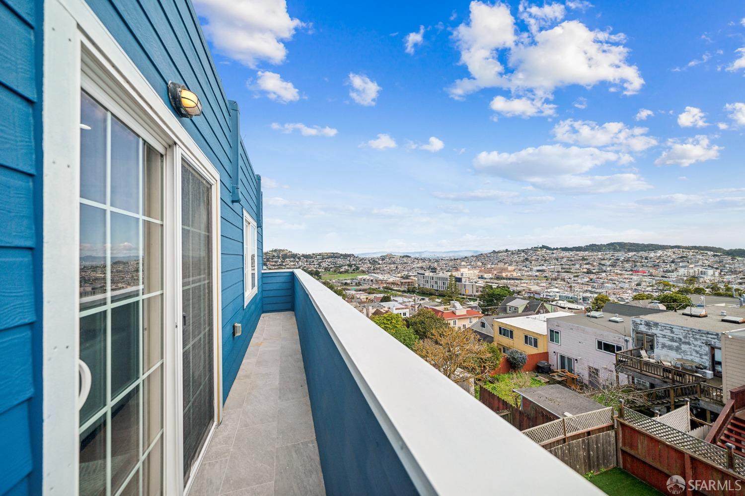 Tiled balcony on a blue-sided home overlooks a dense city neighborhood.