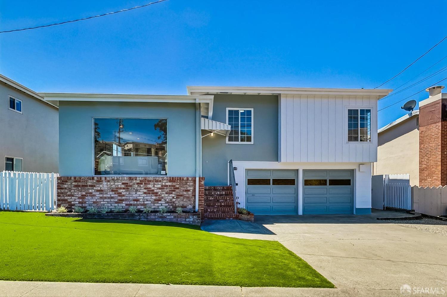 Two-story blue-gray and white home with twin garage doors, brick facade, and green lawn.