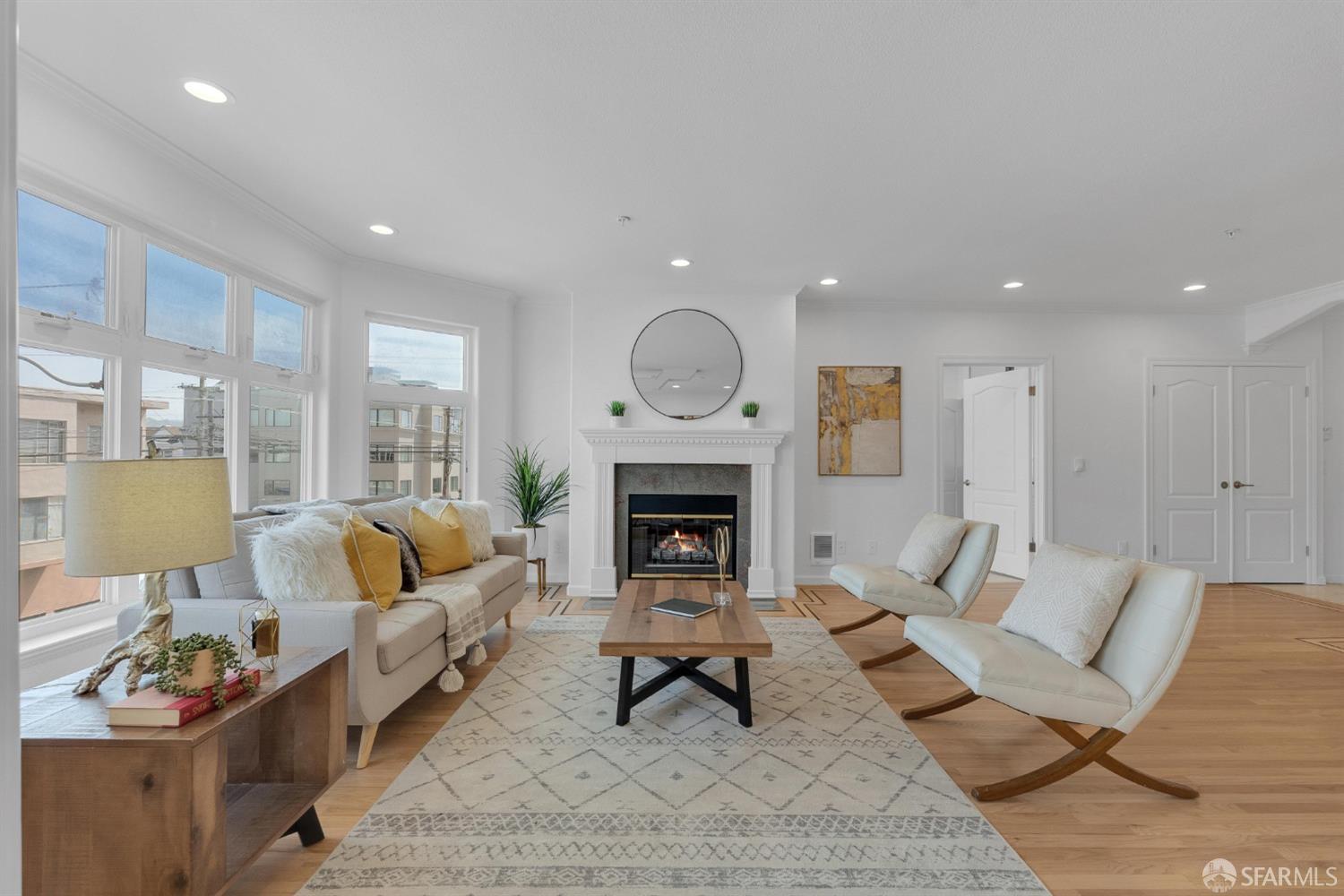 Bright living room with a white fireplace, large windows, and neutral seating with yellow accent pillows.
