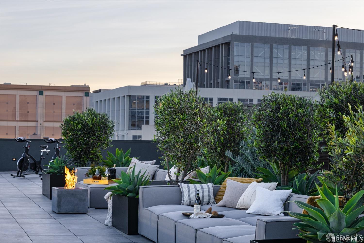 Rooftop deck with lounge seating, potted greenery, string lights, and a gas fire feature.