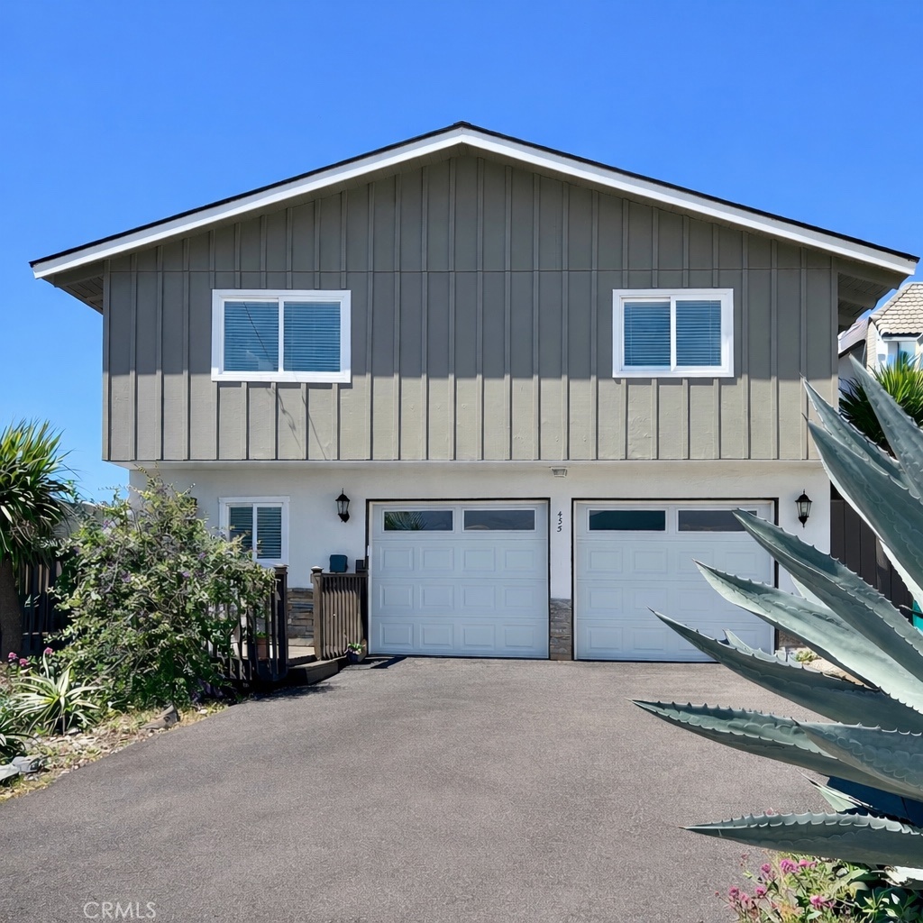 Two-story gray home with two garage doors and a broad driveway, framed by agave plants.