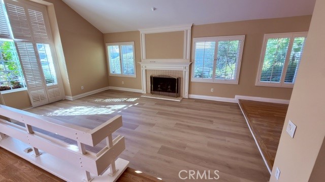 Vacant living room with a fireplace, plantation shutters, and wood flooring.