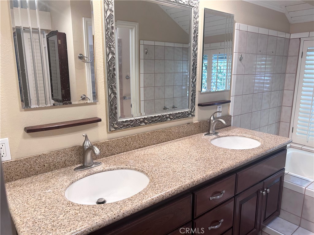 Bathroom with a double-sink granite vanity, dark wood cabinets, and tiled tub and shower.