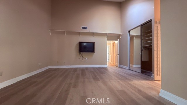 Empty bedroom with wood flooring, a wall-mounted television, and an open closet.
