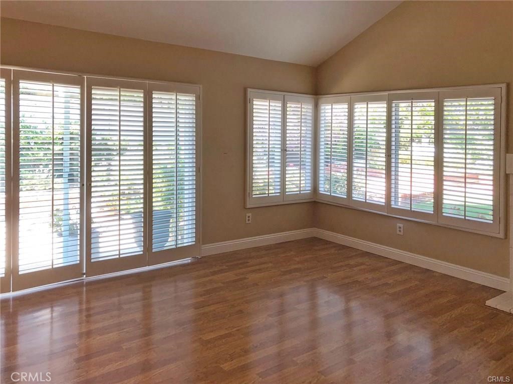 Empty room with hardwood floors and white plantation shutters across wide windows and glass doors.