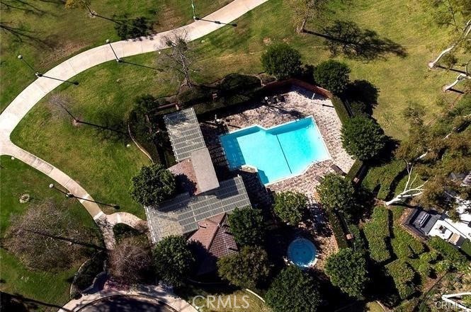 Aerial view of a home and bright blue swimming pool amid landscaped grounds and curving walkways.