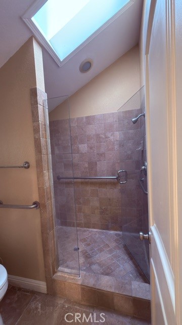 Tiled walk-in shower with a glass enclosure, grab bar, and overhead skylight.