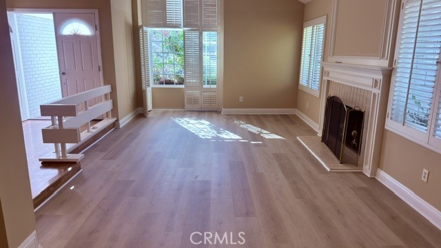 Vacant living room with light wood floors, a fireplace, and shuttered windows.