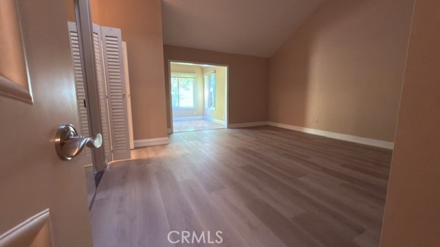 Vacant bedroom with wood-look floors and louvered closet doors, opening to a bright adjoining room.