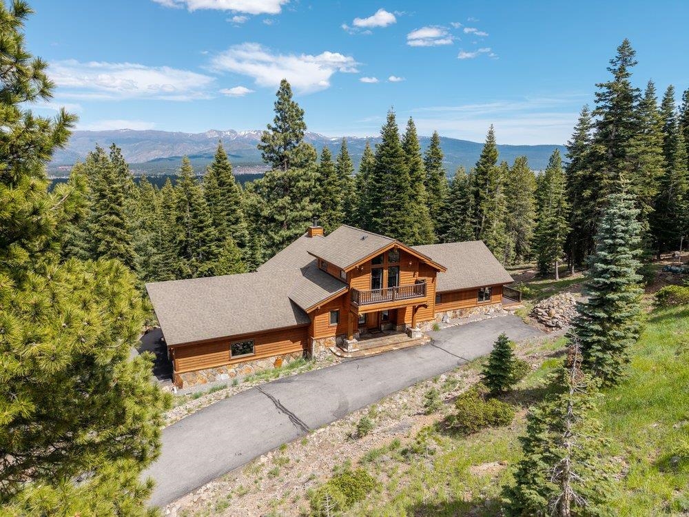 Aerial view of a wood-sided mountain home among pines, with a distant mountain range.