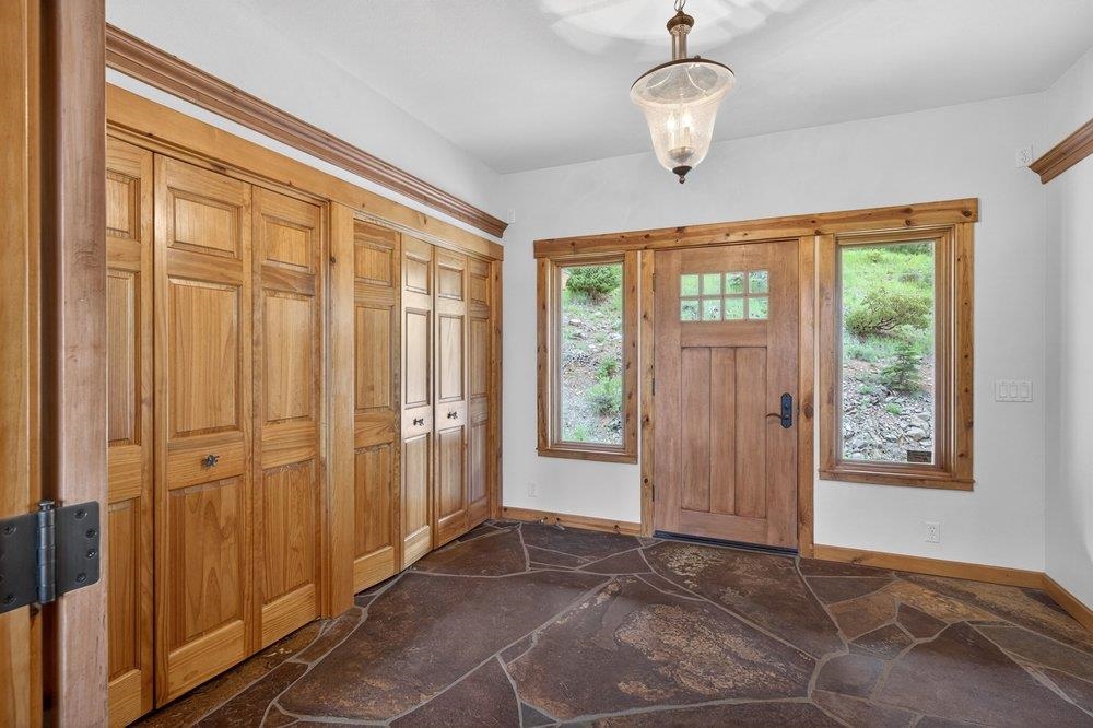 Entryway with a wood front door, tall windows, built-in cabinets, and an irregular stone tile floor.