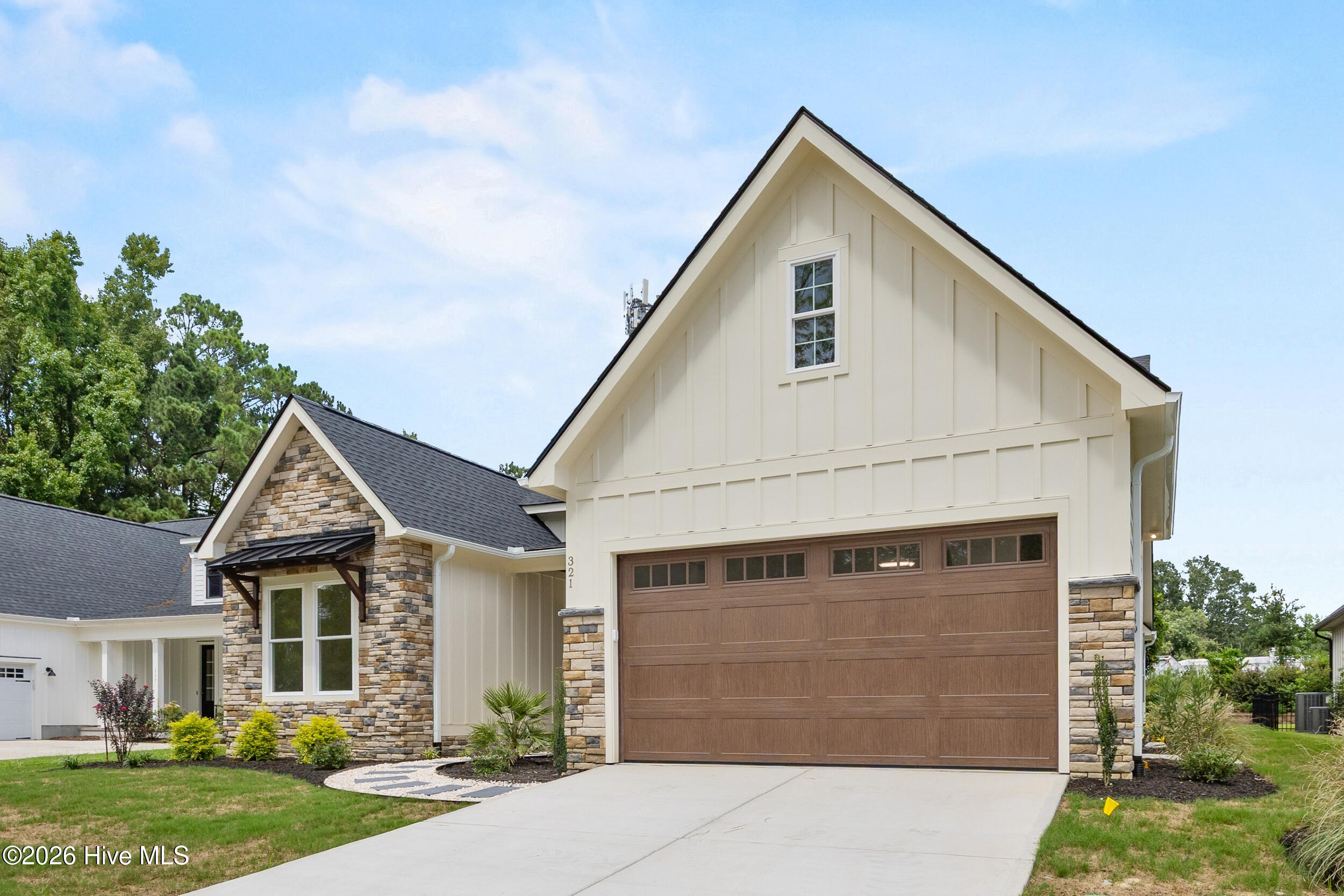 Cream gable-front home with stone accents, brown garage door, and landscaped driveway.