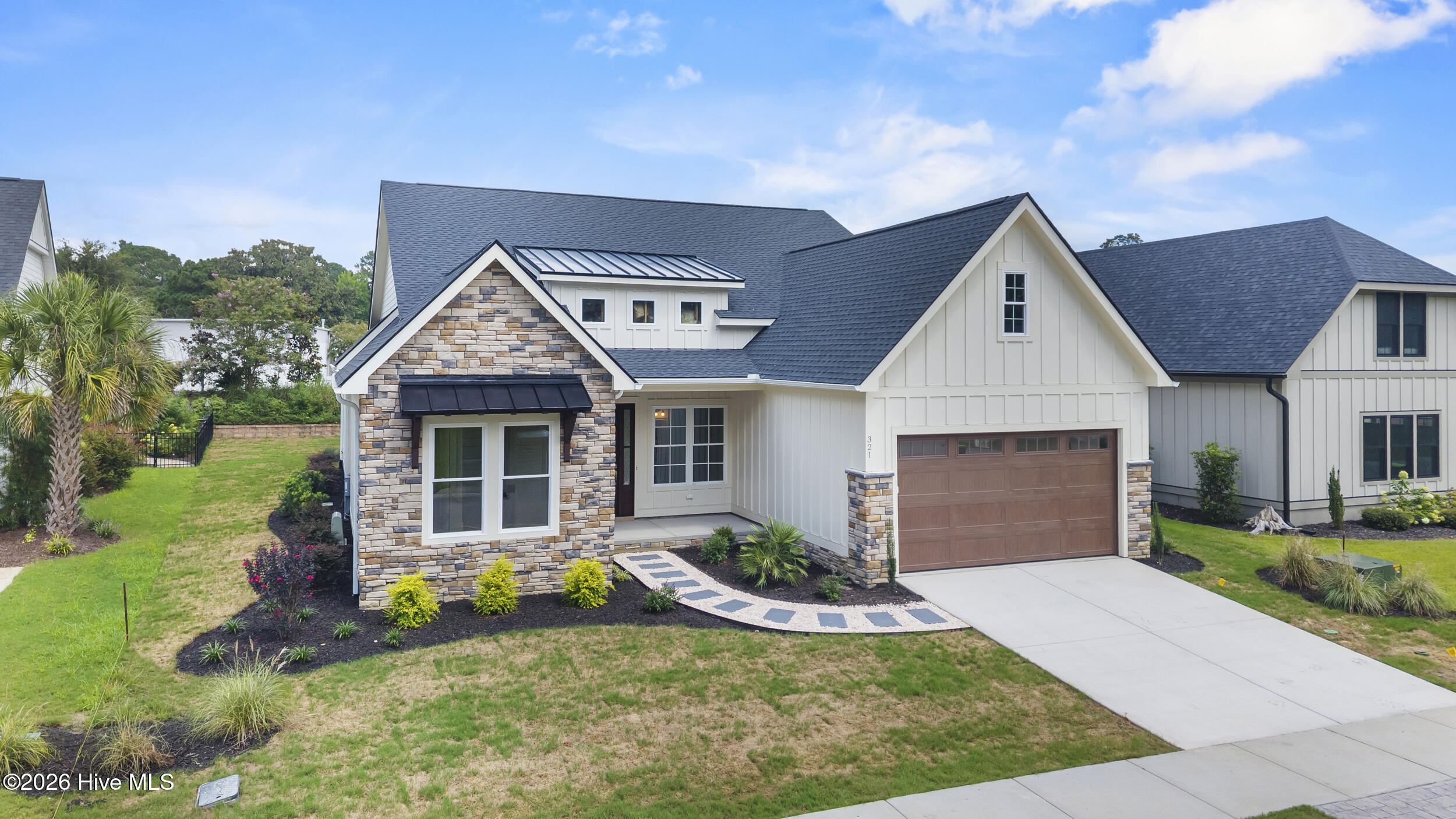Modern white home with stone accents, brown garage door, landscaped lawn, and curved entry walkway.
