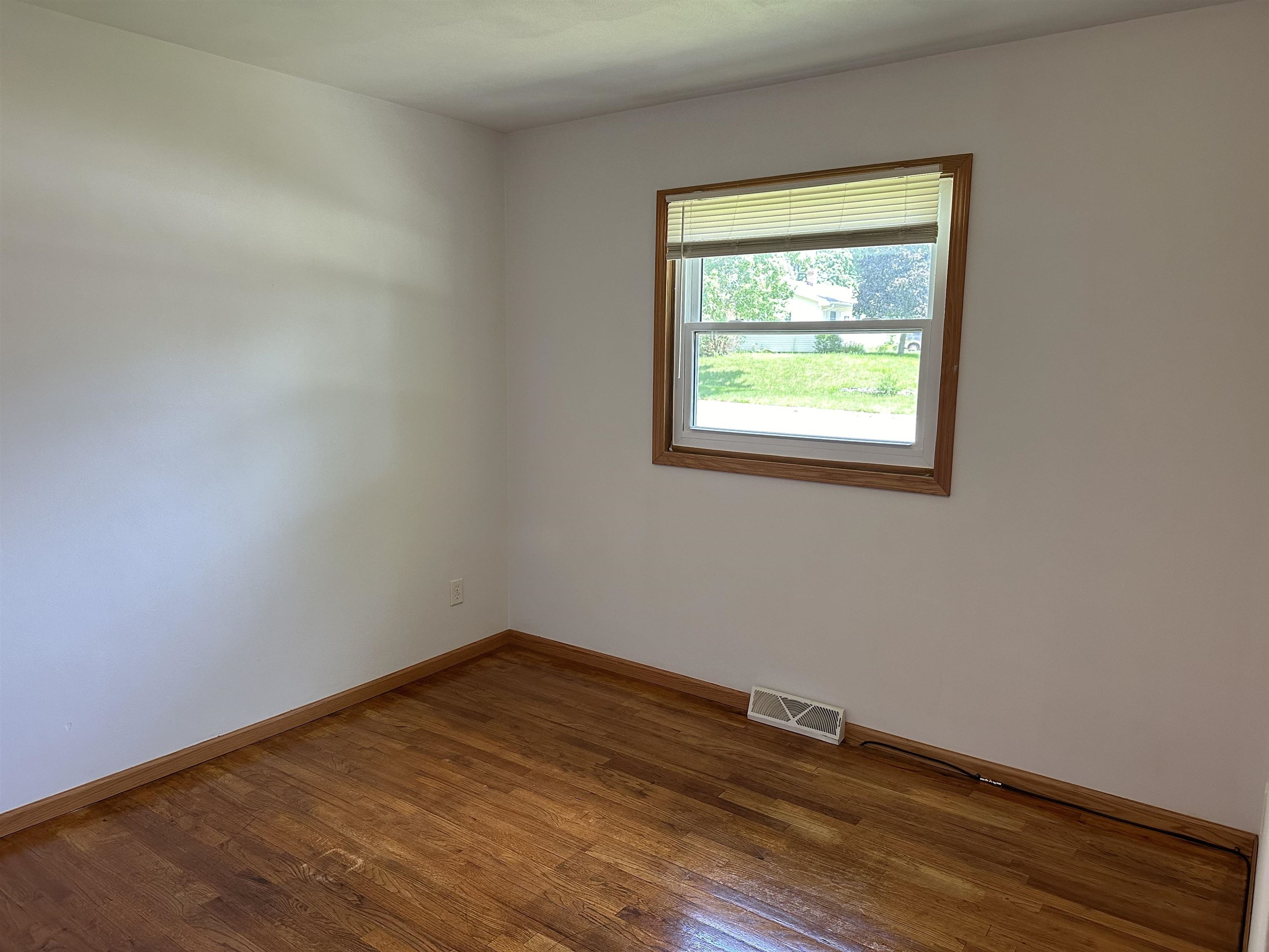Empty room with hardwood floors and a window with blinds.