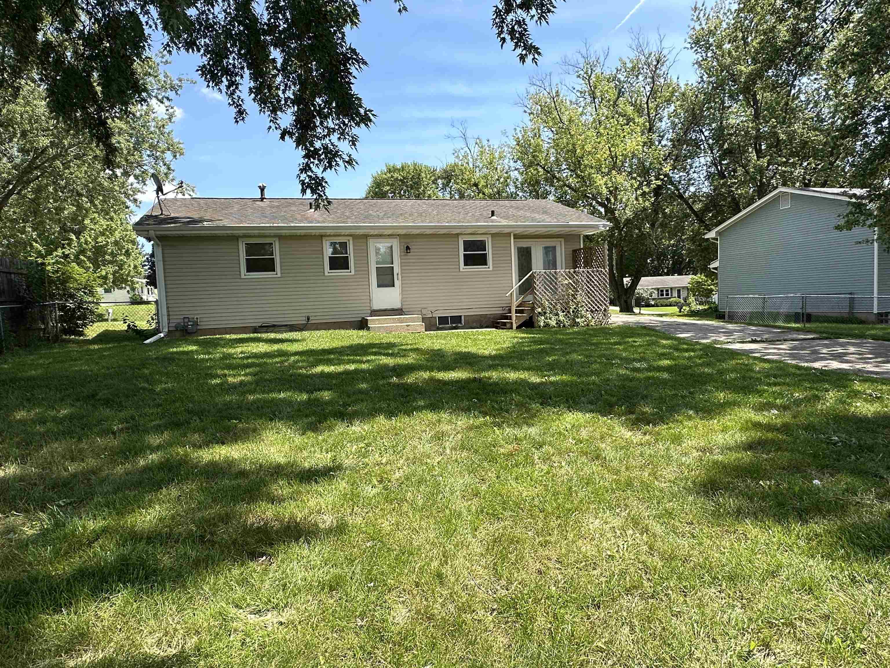 Rear of a single-story beige home with wooden steps, lattice, and a shaded grassy yard.