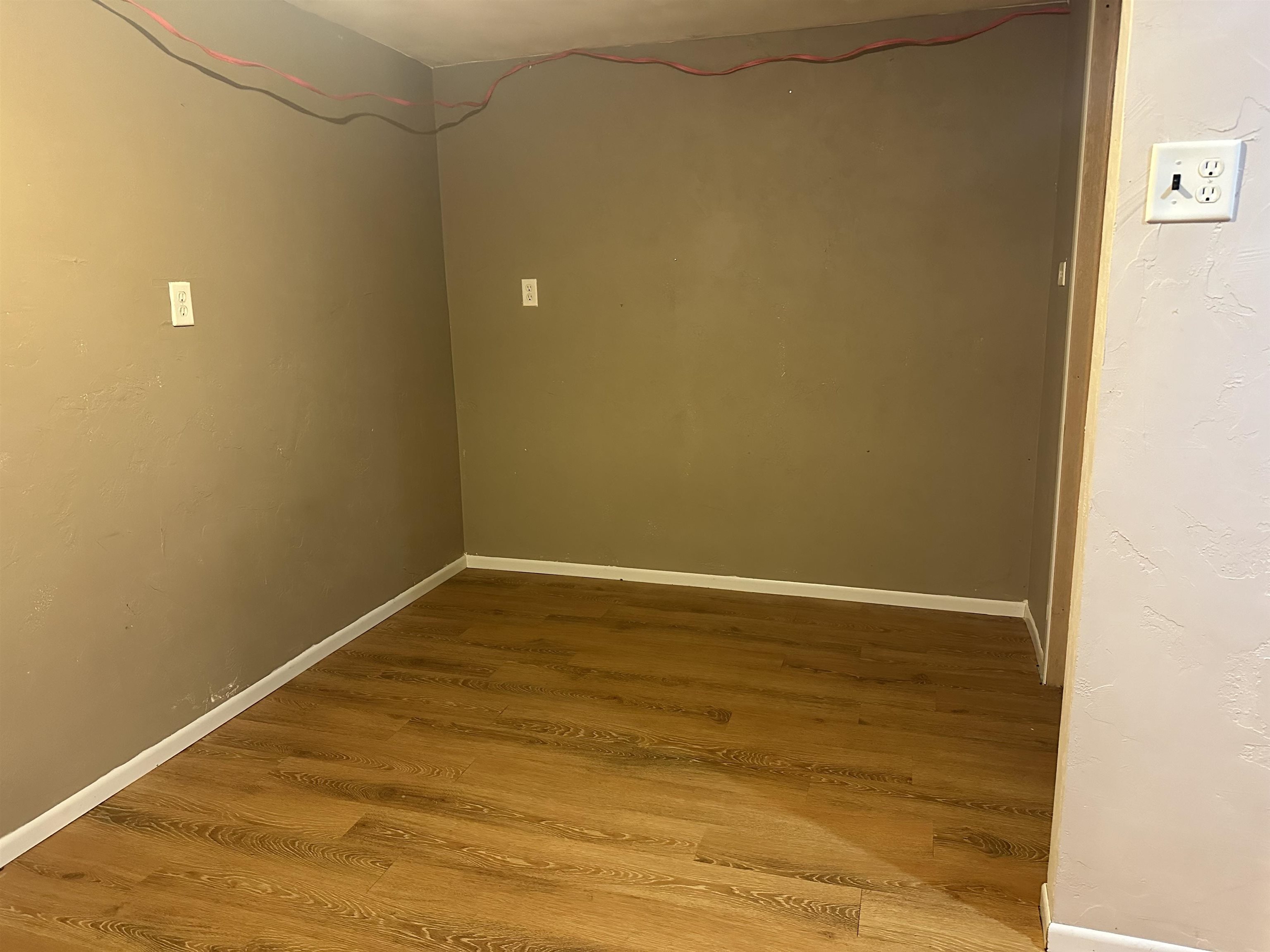 Empty room with brown walls, wood-look plank flooring, and exposed wires along the ceiling.