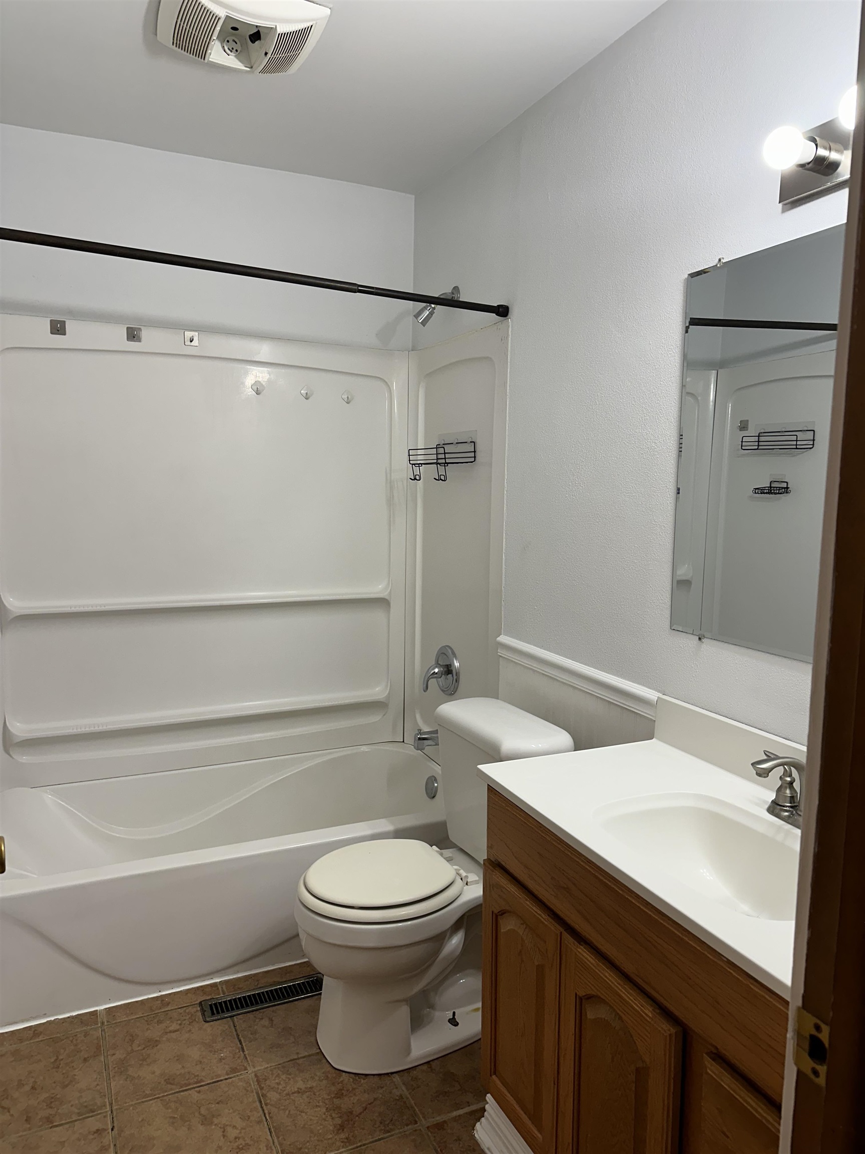 Bathroom with a white tub-shower, toilet, and wood vanity with a white countertop.