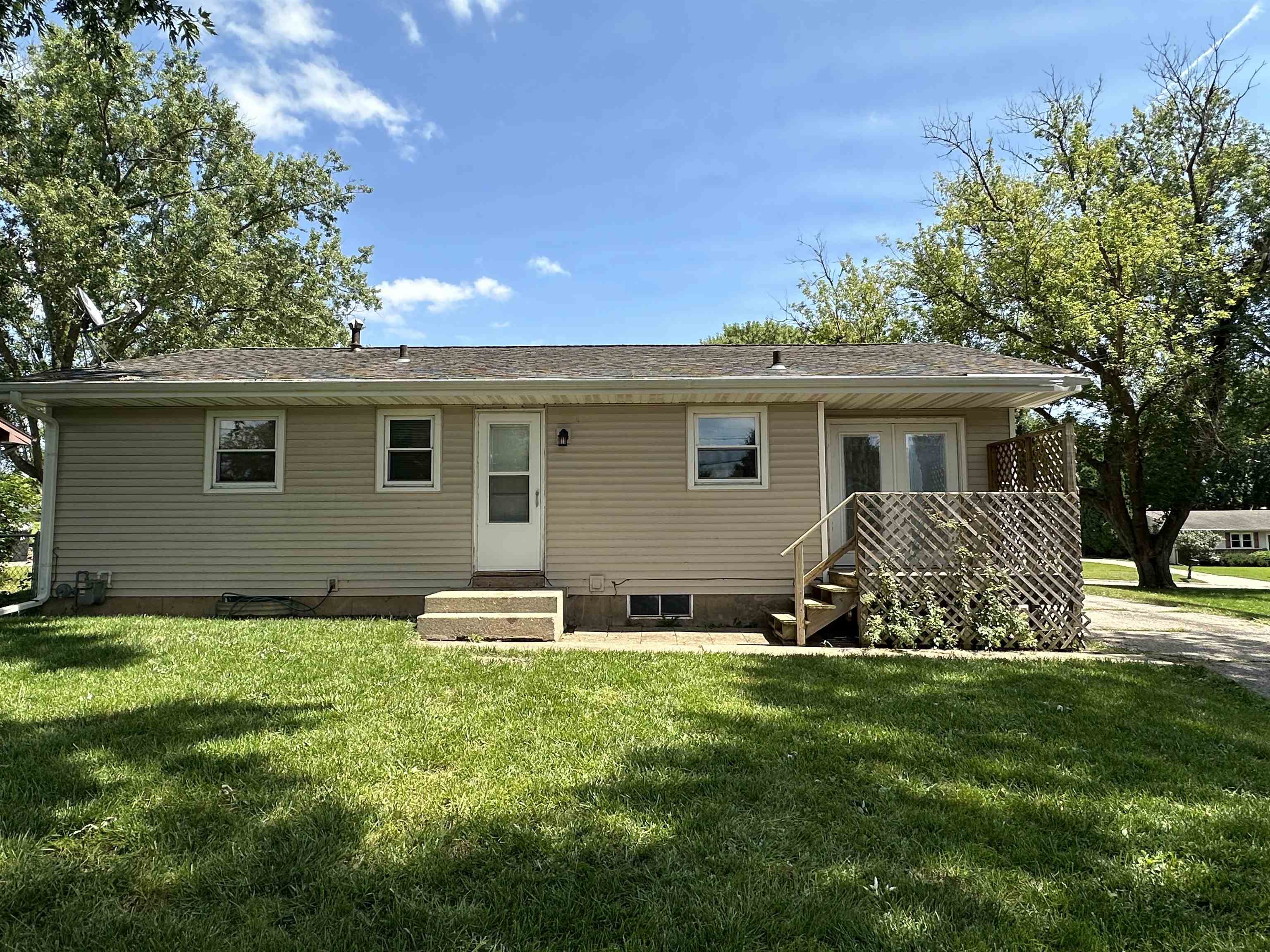 Rear of a single-story beige home with a lattice-sided deck and broad green lawn.